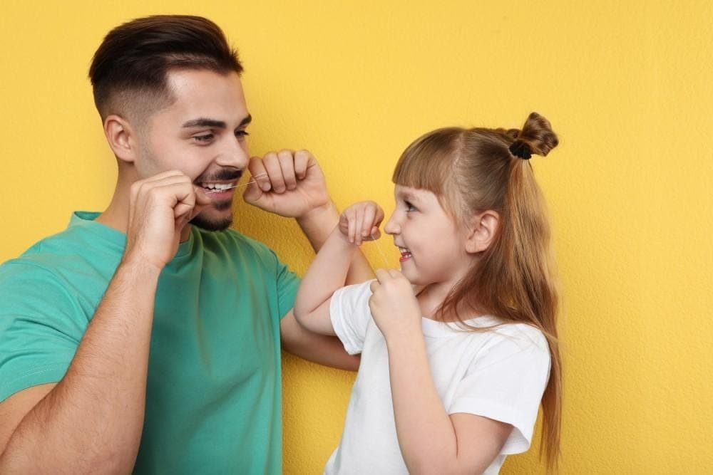 Father and daughter flossing their teeth together