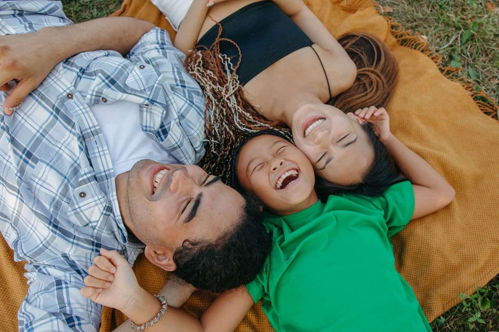 A family lying together on a picnic blanket, laughing