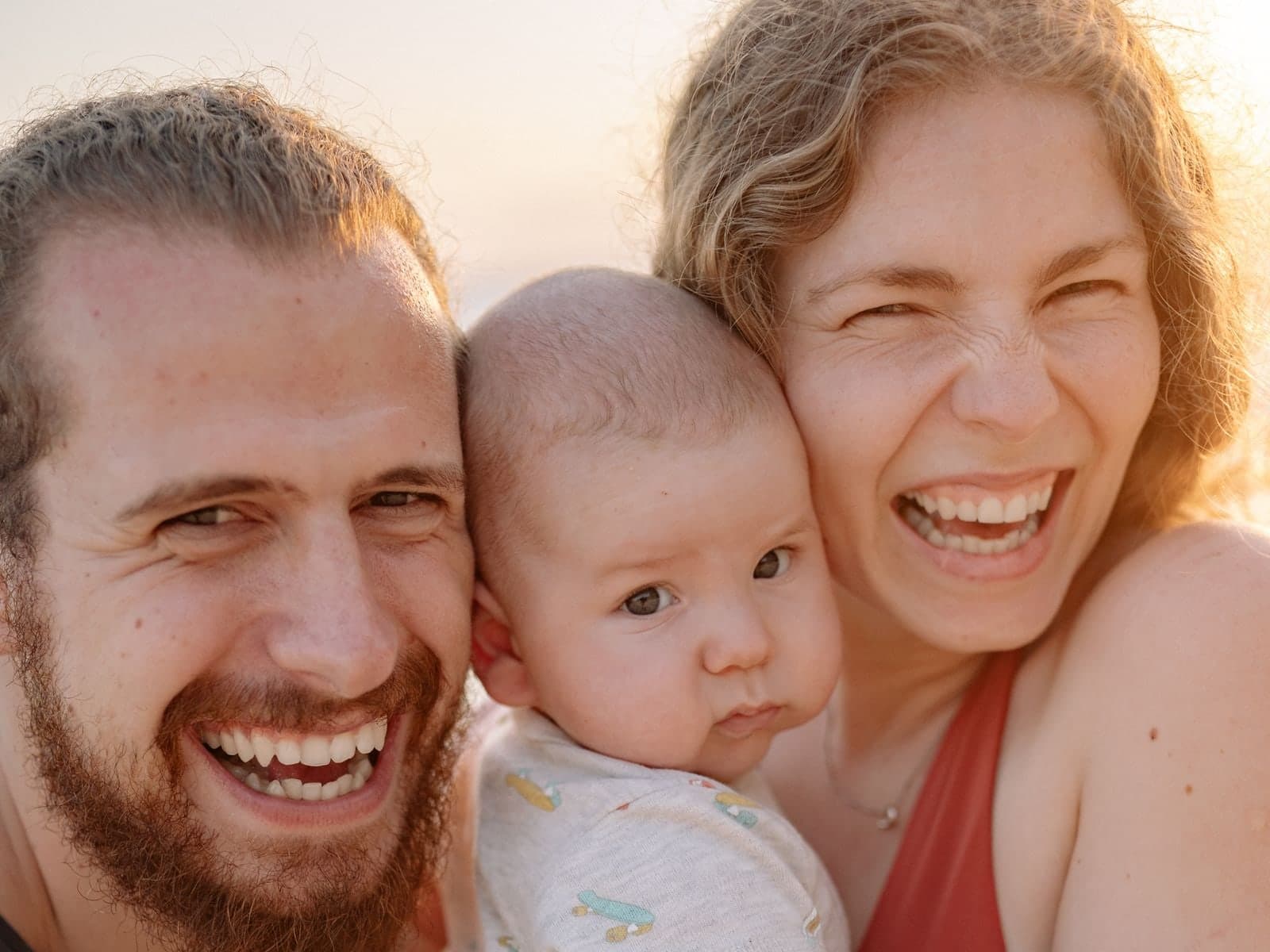 Two parents laughing with their baby in warm evening light